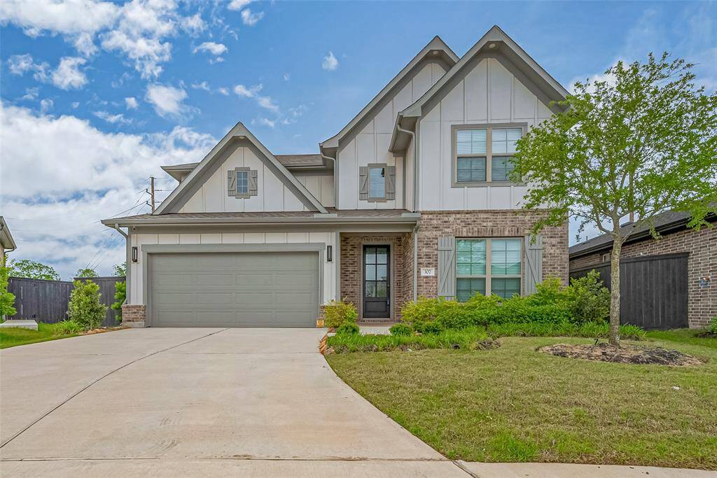 This is a modern two-story house featuring a combination of brick and siding exterior. It includes a spacious driveway leading to a tandem garage, and a well-maintained front lawn with an oak tree and shrubs. The architecture is clean and inviting, perfect for a family home.