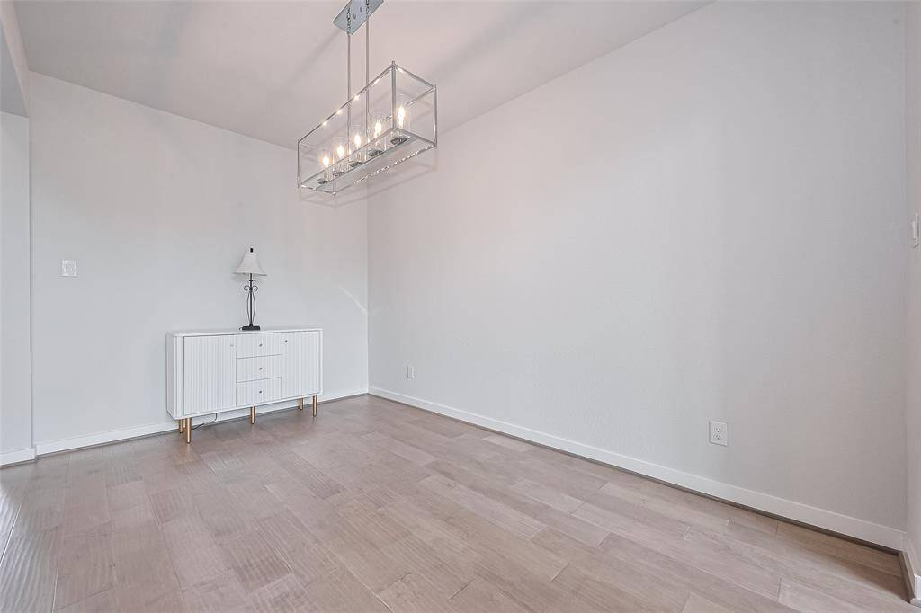 This room features a modern, minimalistic design with light wood flooring and neutral walls. It includes a stylish chandelier and a small sideboard with a lamp, offering a clean and inviting space.