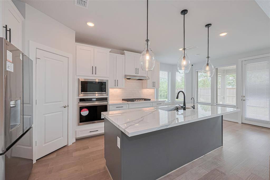 This modern kitchen features sleek stainless steel appliances, a large island with pendant lighting, and ample cabinet space. The open layout and large windows provide plenty of natural light, creating a bright and inviting atmosphere.