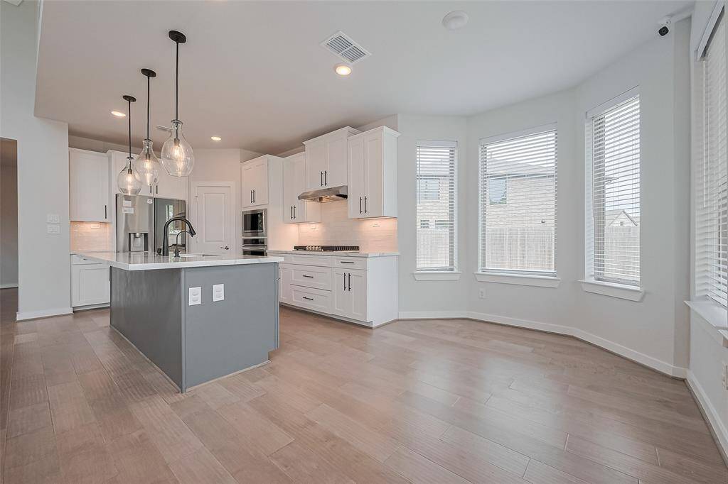 This photo showcases a modern kitchen with a sleek island featuring pendant lighting. It has ample natural light from large windows, white cabinetry, and stainless steel appliances, creating a bright and airy space.