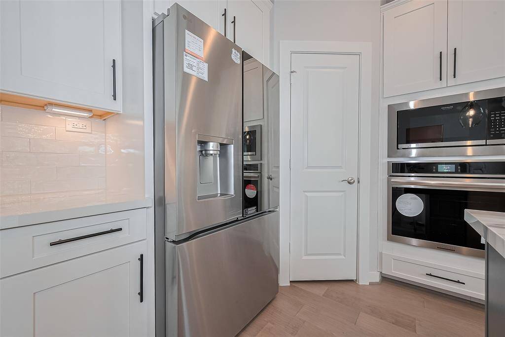 Includes a refrigerator and built-in microwave and oven. It has clean white cabinetry with black hardware, light wood flooring, and a bright, contemporary design.
