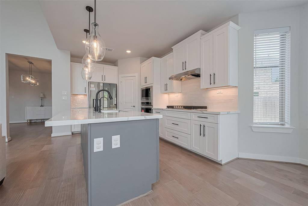 Features sleek white cabinetry, a central island, elegant pendant lighting, stainless steel appliances, a gas cooktop, and ample counter space, all enhanced by natural light from a nearby window.