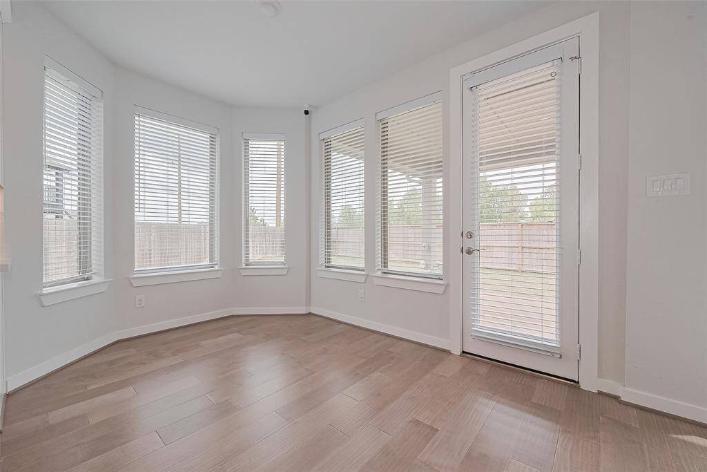 Bright room with large windows and a glass door, offering plenty of natural light. It features light wood flooring and a view of the fenced backyard, ideal for a breakfast room.