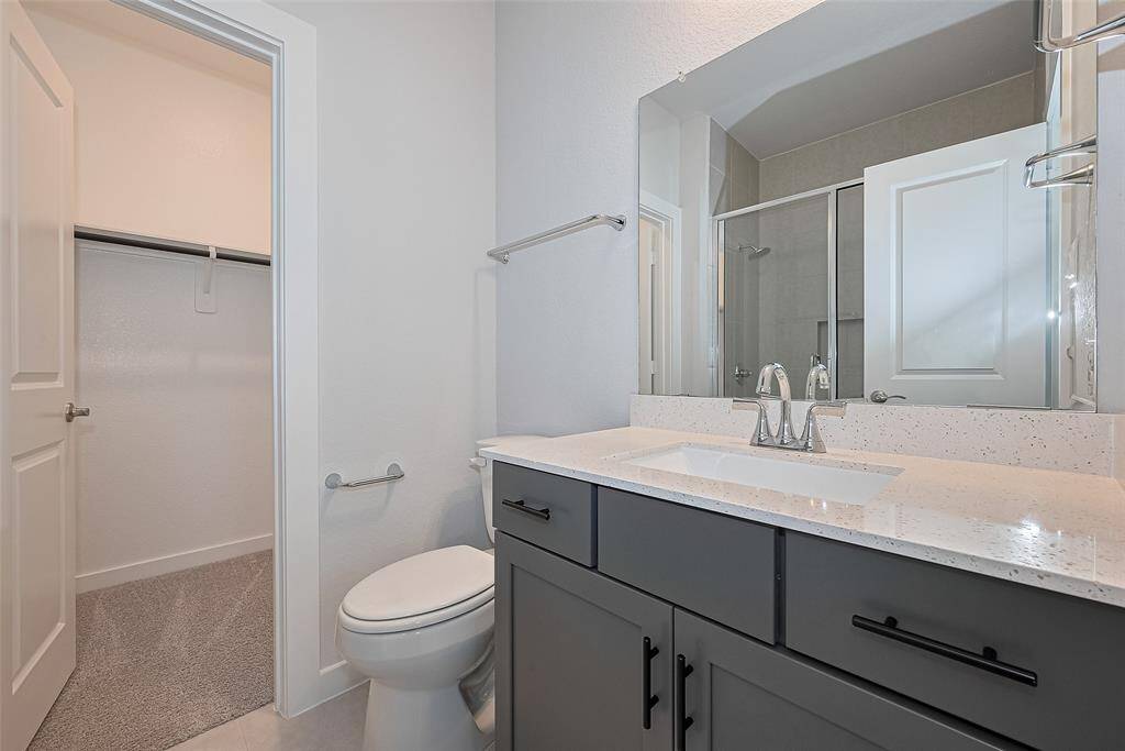 This bathroom features a sleek modern design with a large mirror, a spacious vanity with ample storage. Adjacent is a walk-in closet with carpeted flooring, providing convenient storage.