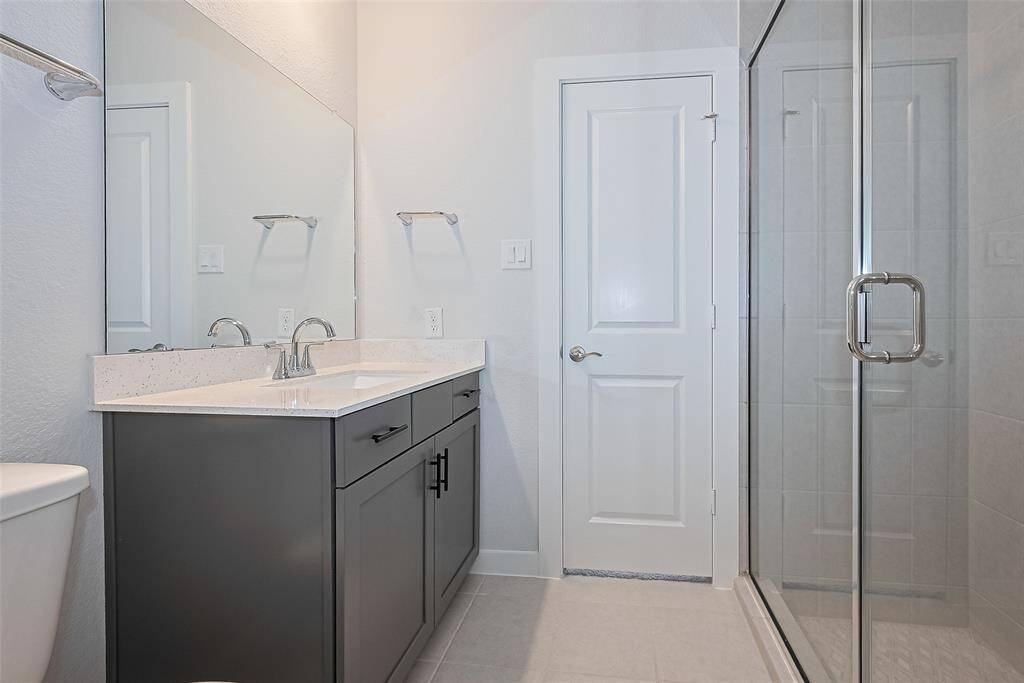 This bathroom features a modern design with a sleek vanity, quartz countertop, large mirror, and glass-enclosed shower. The neutral tones and clean lines create a fresh and inviting space.