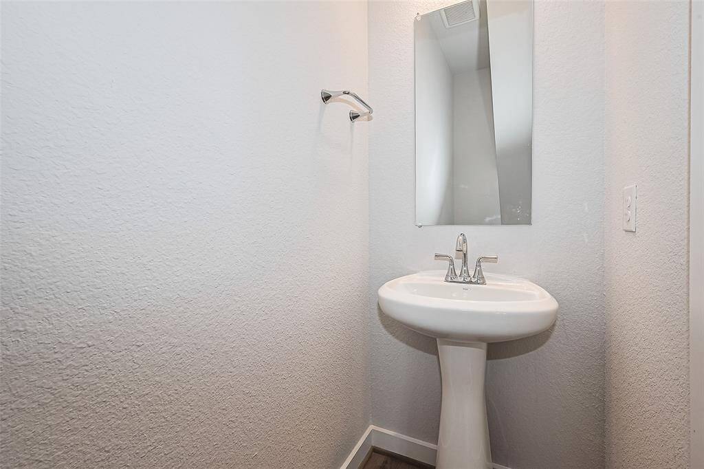 A compact powder room features a sleek pedestal sink, wall-mounted mirror, and contemporary fixtures, offering a minimalist and functional design.
