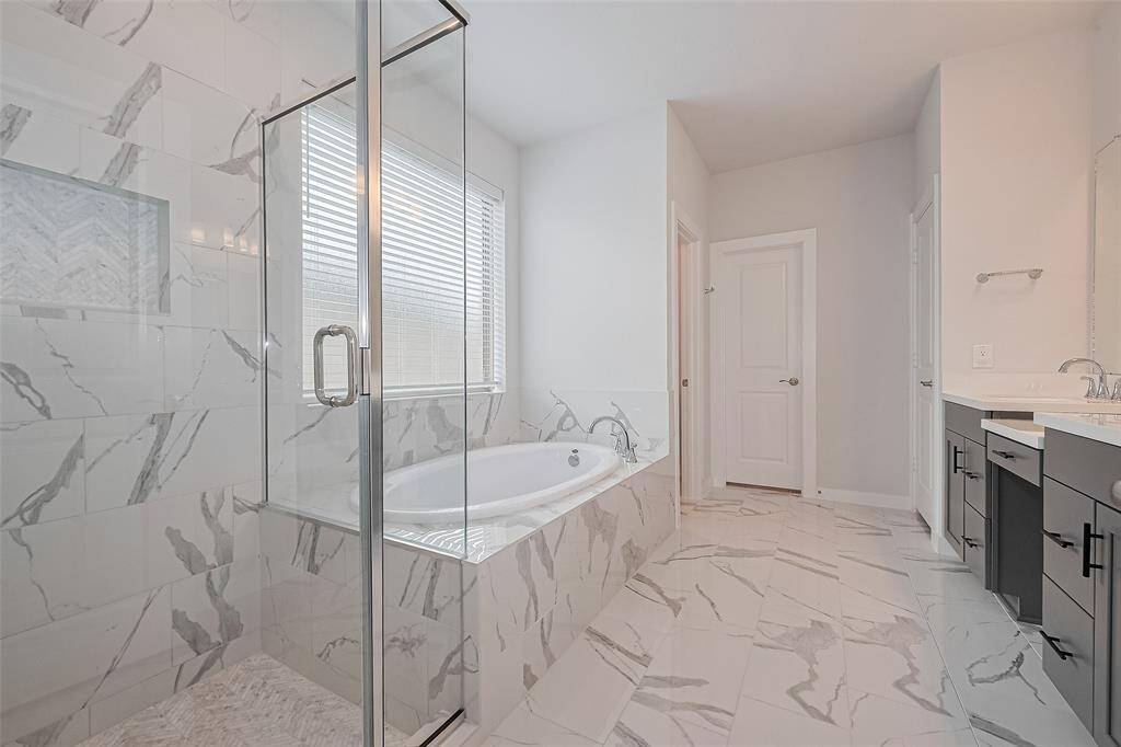 This modern bathroom features elegant marble tile flooring and walls, a spacious glass-enclosed shower, and a large soaking tub. It also includes a double-sink vanity with sleek fixtures, creating a luxurious and bright atmosphere.