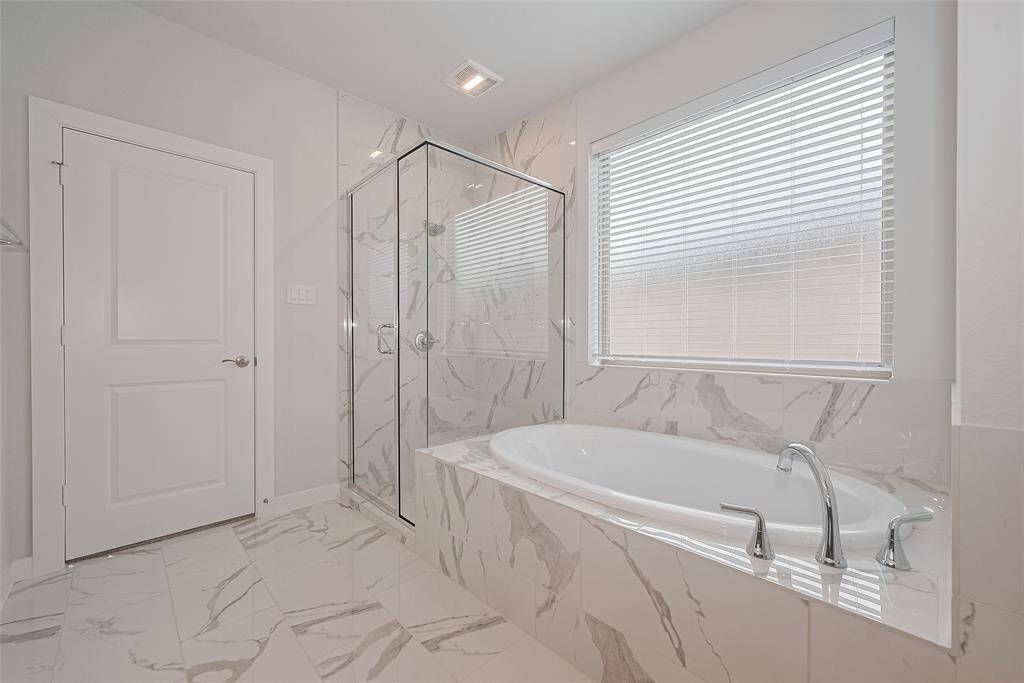 A spacious, modern design with a large soaking tub and a sleek glass-enclosed shower. The marble-style tiles and ample natural light create a luxurious and inviting atmosphere.