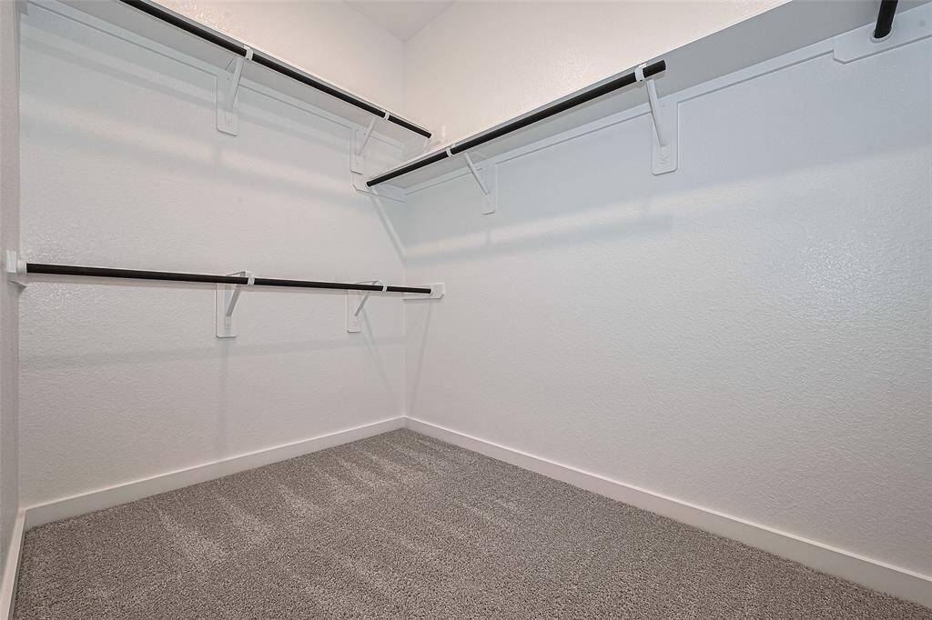 Spacious walk-in closet with multiple shelves and hanging rods, featuring clean white walls and plush carpeting, ideal for organized storage and easy access to clothing and accessories.