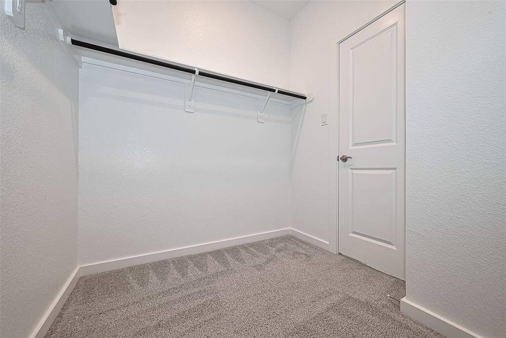 Clean white walls and carpeted flooring, hanging rod and shelf, with a standard door for entry.