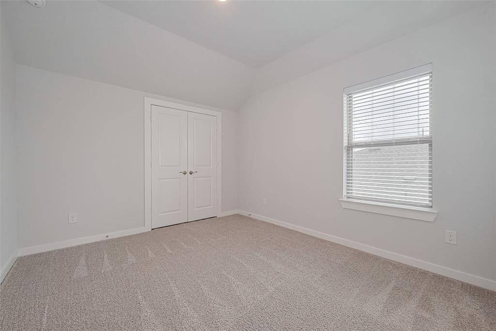 This room features neutral-colored walls and carpet, a window with blinds, and a double-door closet, creating a clean and versatile space.