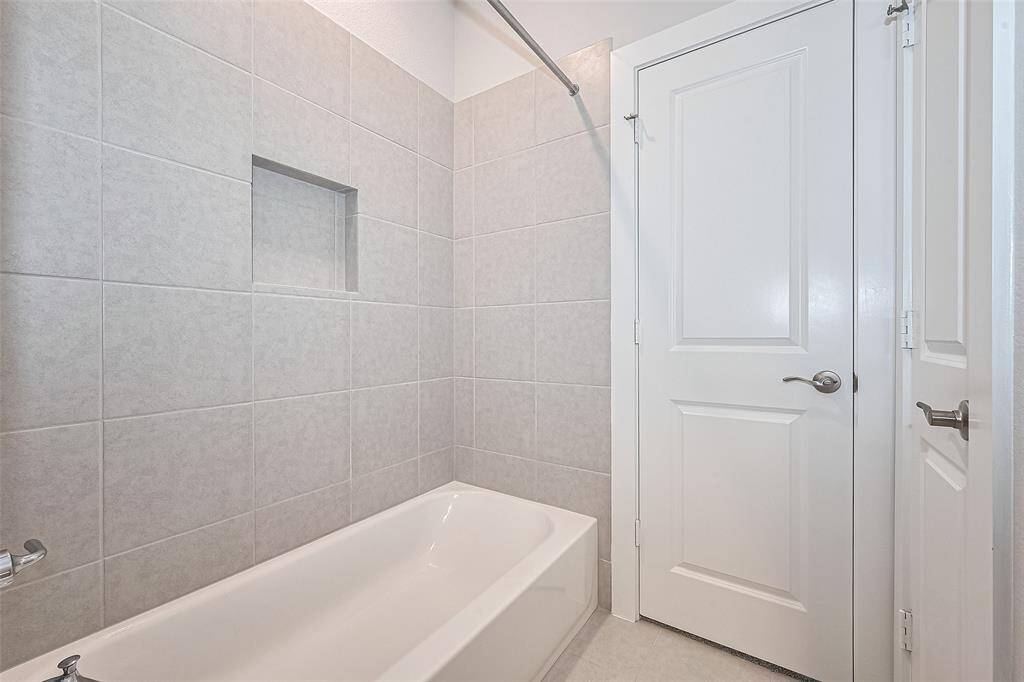 Modern bathroom with a sleek, tiled shower-bath combination, featuring a built-in niche for storage. Bright and minimalistic design with a white door and chrome fixtures.