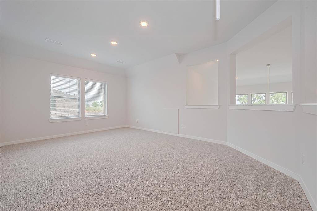 Features neutral carpeting and walls, recessed lighting and windows that let in natural light. An open wall with cutouts provides a view into an adjoining space, enhancing the open feel.