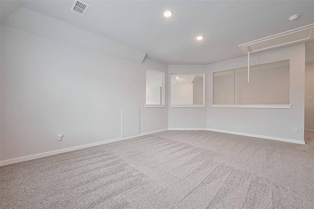 This room features clean, neutral-colored walls and fresh carpeting, creating a bright and versatile space. Recessed lighting and a built-in ceiling access panel add functionality. The layout includes wall cut-outs for a modern, open feel.