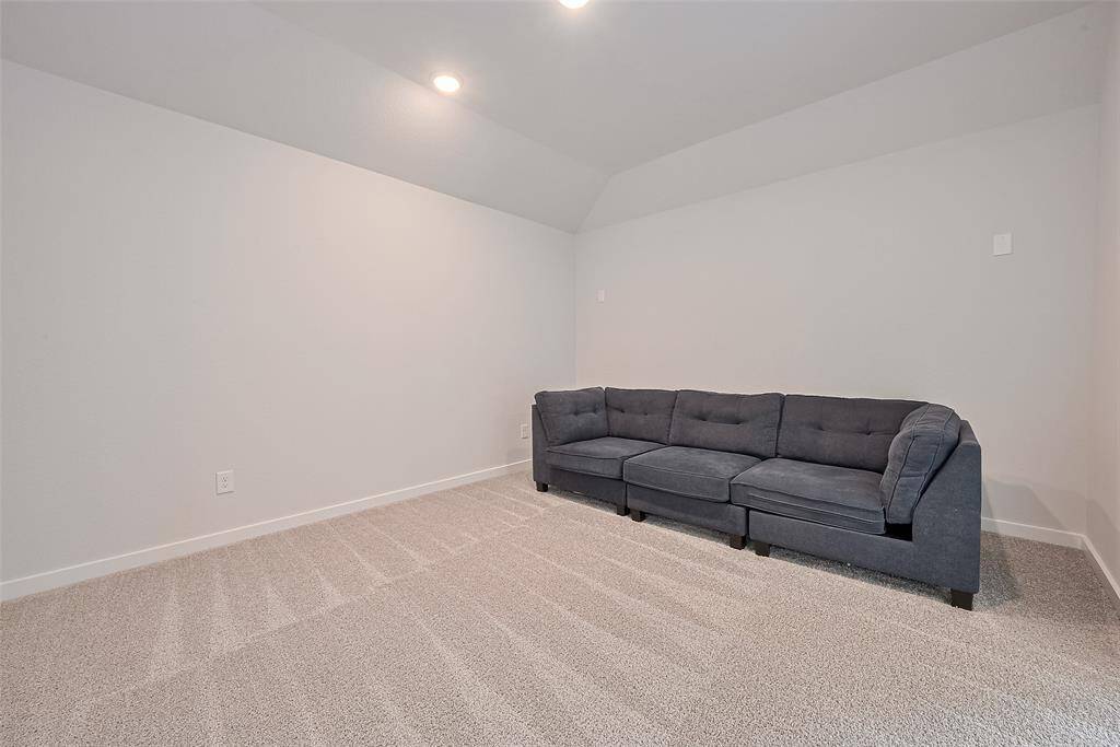 This media room features a modern, carpeted space with neutral walls and recessed lighting, perfect for relaxation. A comfortable sofa provides seating, making it an ideal cozy corner for entertainment or lounging.