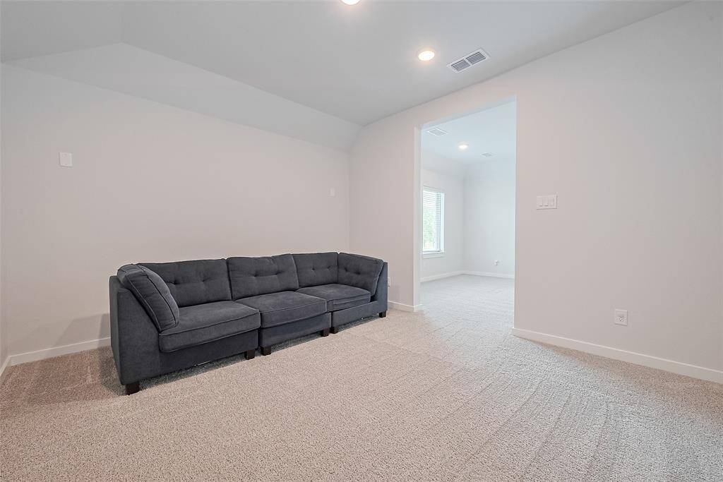 Media room has a bright, carpeted room with a modern gray sofa and recessed lighting.