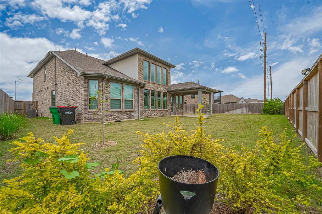 The yard is fenced, offering privacy, and includes some landscaping with bushes and some trees.