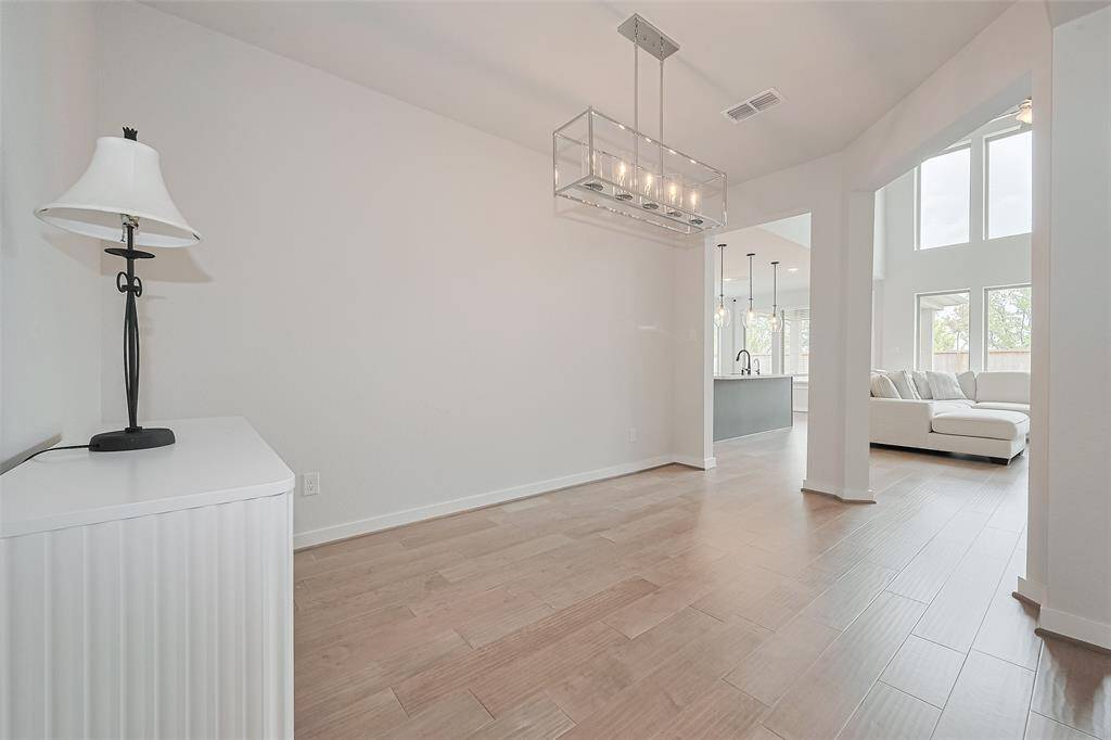 This bright, open space features modern wood flooring and high ceilings. A contemporary chandelier enhances the dining area, while large windows in the adjacent living room provide ample natural light. The layout seamlessly connects to a stylish kitchen, perfect for entertaining.