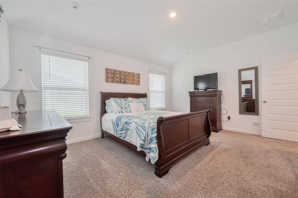 The primary bedroom is filled with natural light from large windows and softly illuminated by recessed lighting overhead.