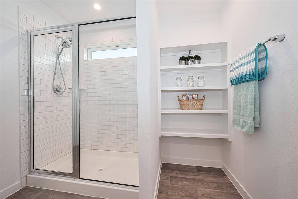 The primary bathroom features a glass-enclosed shower with adjacent built-in shelving for ease and organization.