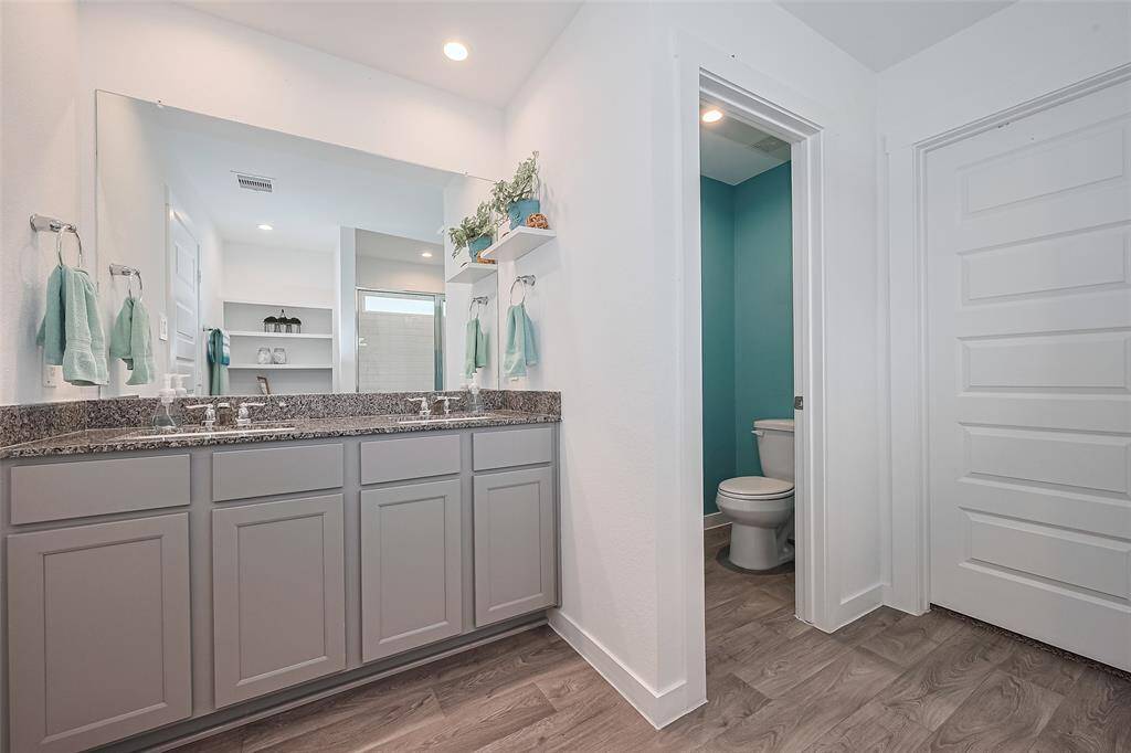 A dual sink vanity with an expansive mirror sits next to a discreet toilet area tucked away for added privacy.