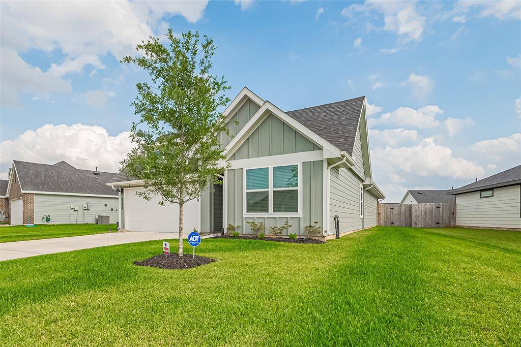 The front yard features a healthy green lawn with a young tree, while a thoughtfully placed plant bed enhances the home’s façade.