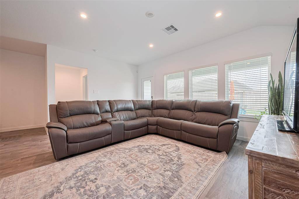 A wall of oversized windows brightens the living room, offering a cheerful backdrop of sunlight and outdoor greenery.