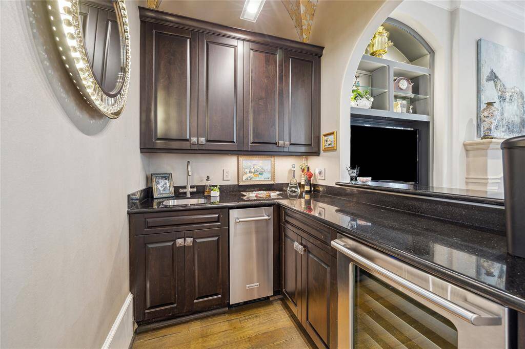 The wet bar, conveniently located just off the living room, features sleek granite countertops, an ice maker, a wine refrigerator, and a large arched window that offers a view into the living room, making it great for entertaining.