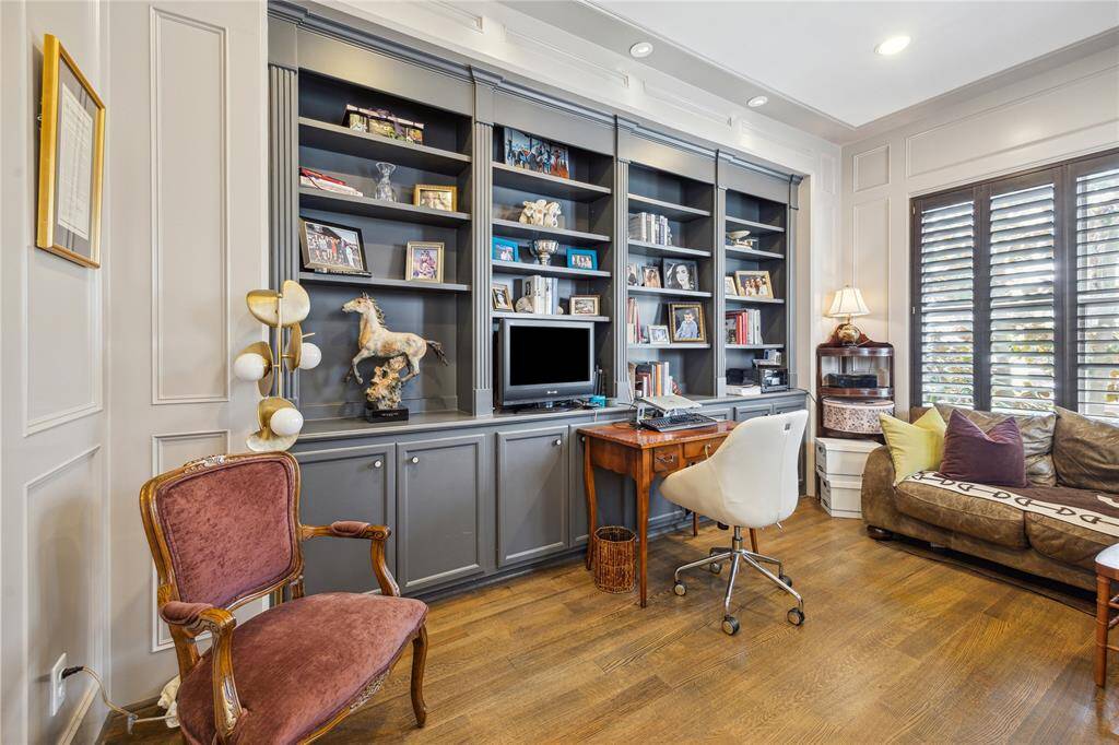 The handsome office features custom built-in cabinetry and shelves, stunning millwork walls, large windows that bring in natural light, and recessed lighting—creating an elegant and functional space just off the primary suite.