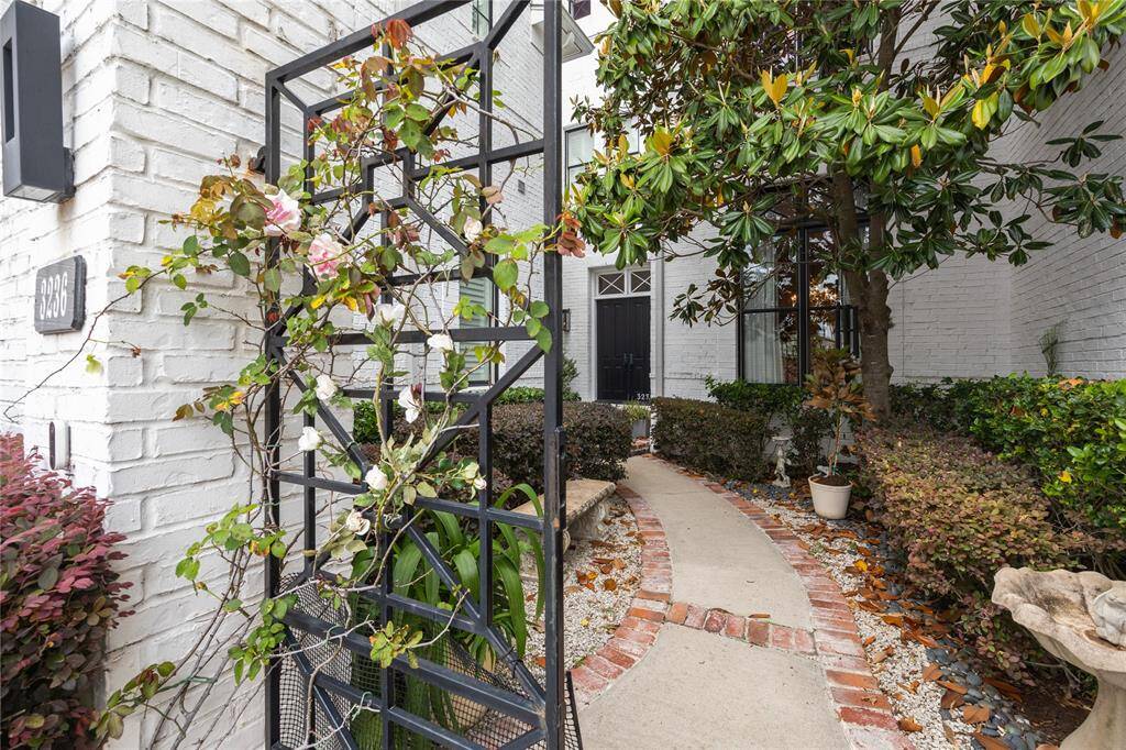 A brick-lined walkway winds through the courtyard, surrounded by well-maintained landscaping, and leads to the front door.