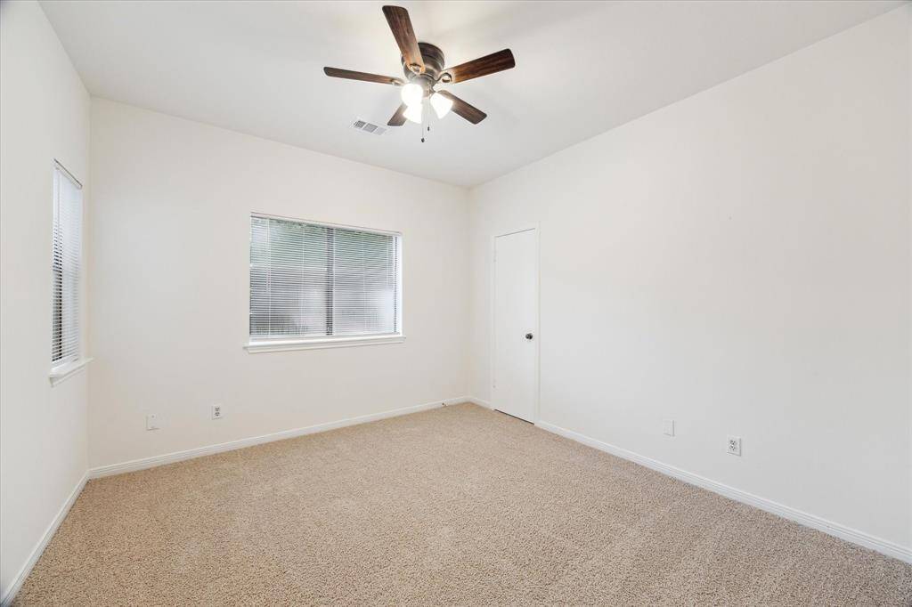 This room features neutral walls, plush carpeting, a ceiling fan with lights, and windows for natural light, creating a bright and cozy atmosphere.