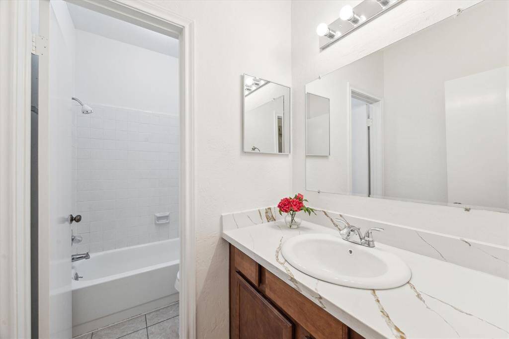 Bright bathroom featuring a bathtub with shower, a modern vanity with updated quartz countertop, and a large mirror.