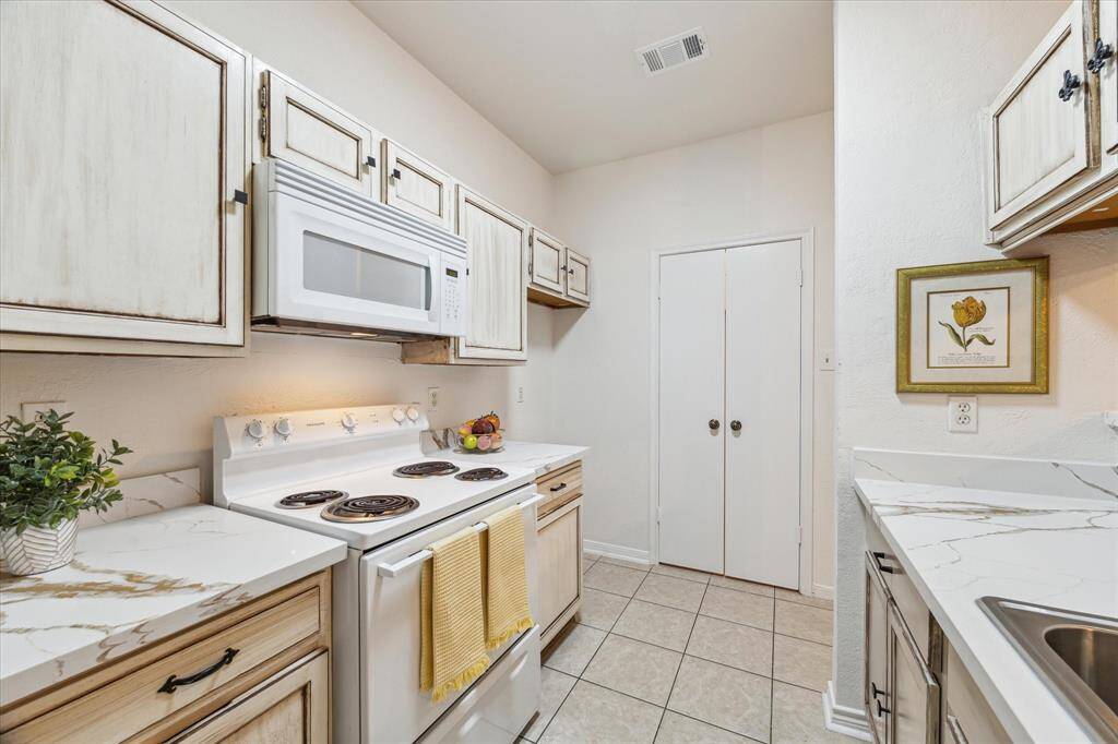 Cozy galley layout with vintage-style cabinetry and updated quartz countertops and modern appliances.