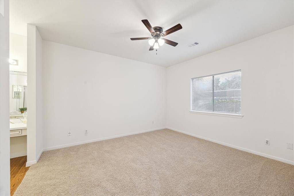 This spacious bedroom features neutral carpeting, a ceiling fan, and a large window for natural light. Freshly painted! It includes an adjacent bathroom with a modern vanity.