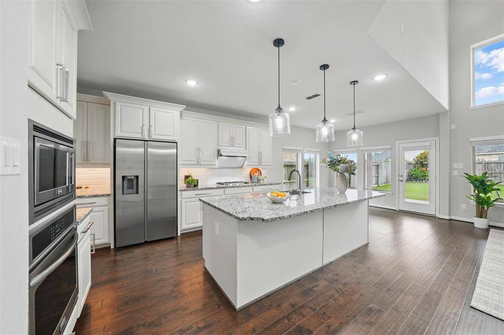 Modern kitchen with granite island and stainless appliances, full of natural light.