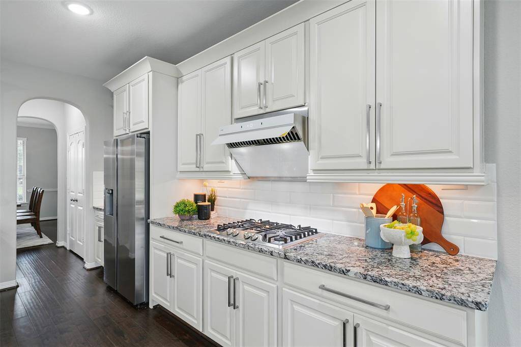 Bright kitchen with granite counters, white cabinets, and stainless steel appliances.