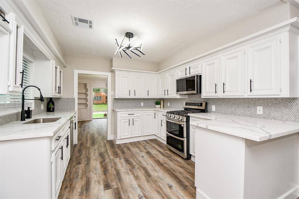 Bright and modern kitchen featuring white cabinetry, sleek quartz countertops, stainless steel appliances,gas stove/ double oven,modern light fixture and neutral backsplash add contemporary flair.
