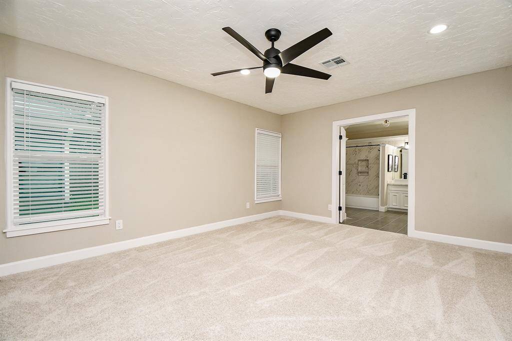 Primary bedroom features 3- Closets, neutral walls, plush carpet, and a modern ceiling fan. It connects to a stylish en-suite bathroom with sleek tile and ample lighting.
