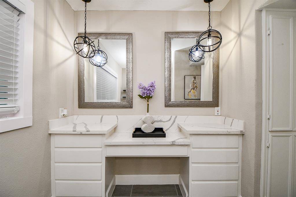 Modern hall bathroom showcases a stylish vanity area featuring dual mirrors with elegant frames, pendant lighting, and a sleek Quartz Countertop. The neutral color palette and decorative accents create a sophisticated and inviting atmosphere.