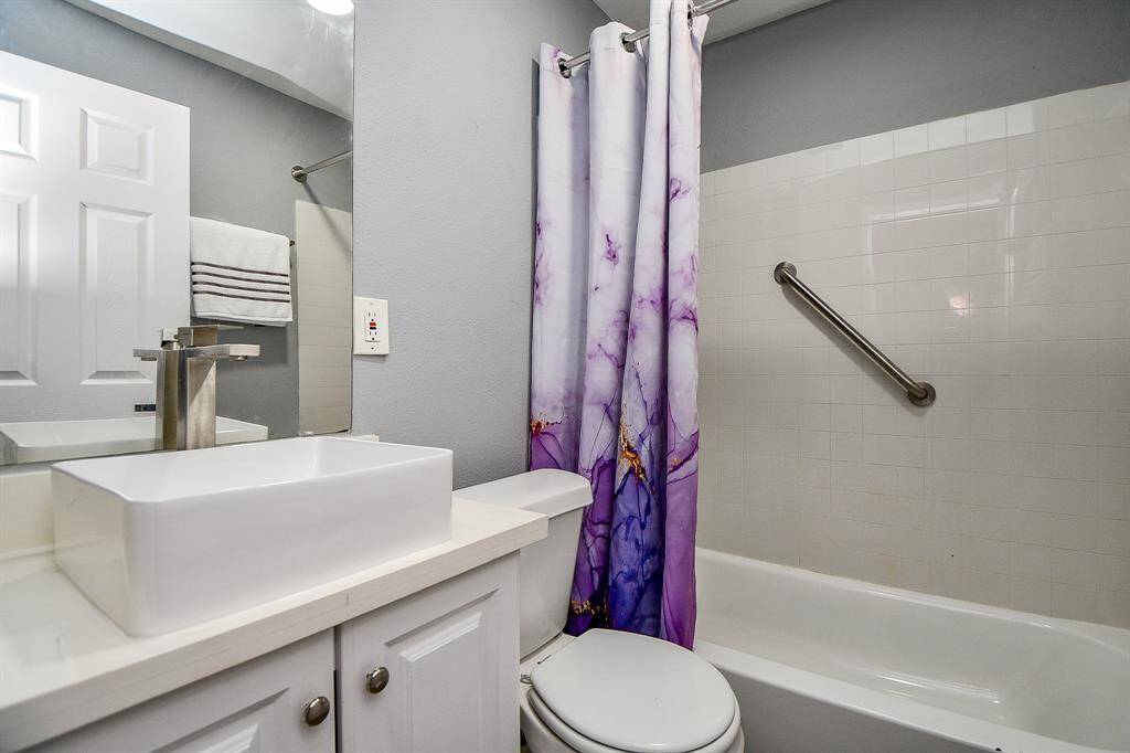 This bathroom in the cottage features a modern white sink with a sleek faucet, a tiled bathtub/shower combo with a safety grab bar.