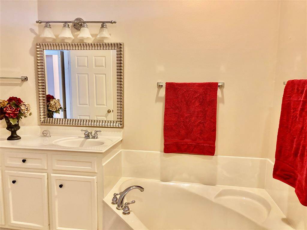 Primary bath with separate sinks, tile flooring, and a corner soaking tub.