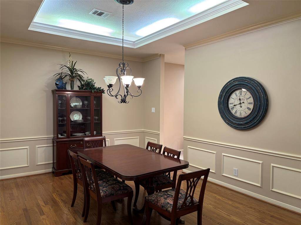Elegant dining room featuring warm wood flooring, chair rail molding, picture frame molding, and tray ceiling lighting, perfect for all your gatherings.