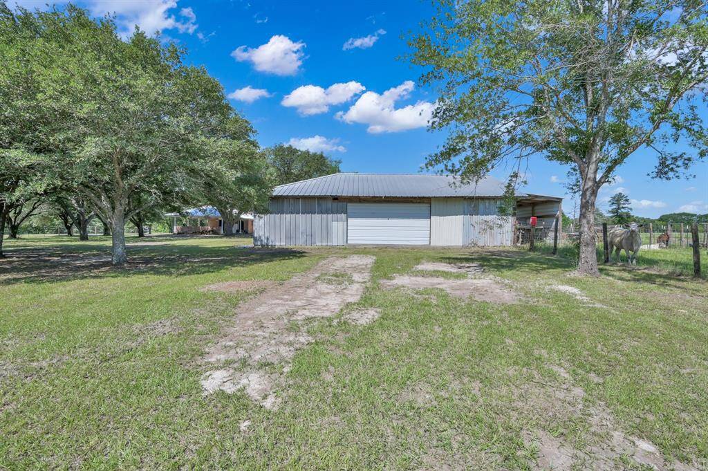 Showcasing a spacious rural property with a large metal barn, surrounded by trees and open grassy areas. Ideal for agricultural use or livestock, the setting is tranquil and expansive.