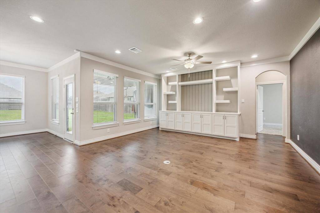 Spacious living area with hardwood floors, abundant natural light from large windows, and built-in shelving for added character.