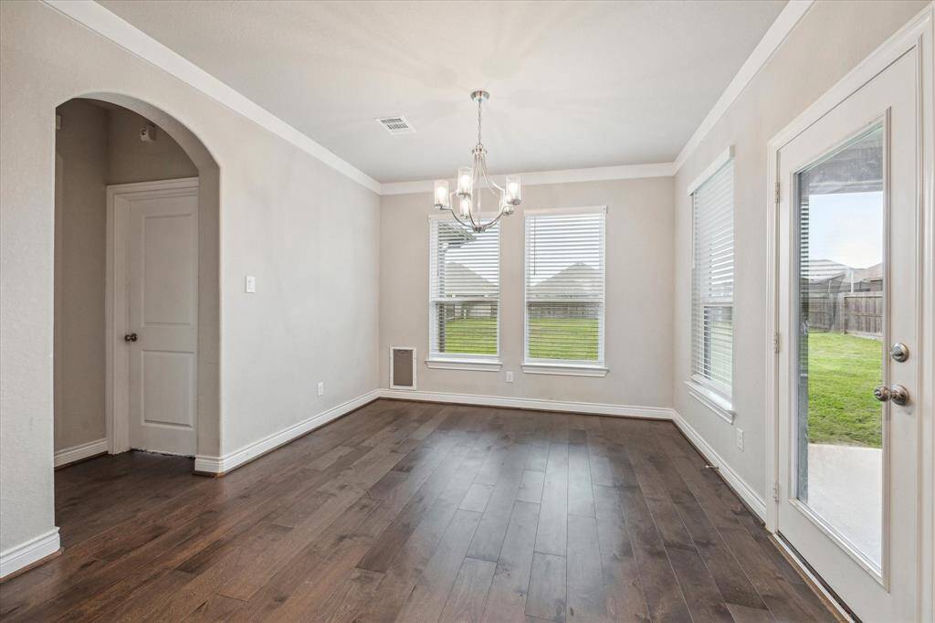 Bright and inviting dining area with elegant hardwood floors, a modern chandelier, and abundant natural light from large windows and a glass door leading to the backyard.