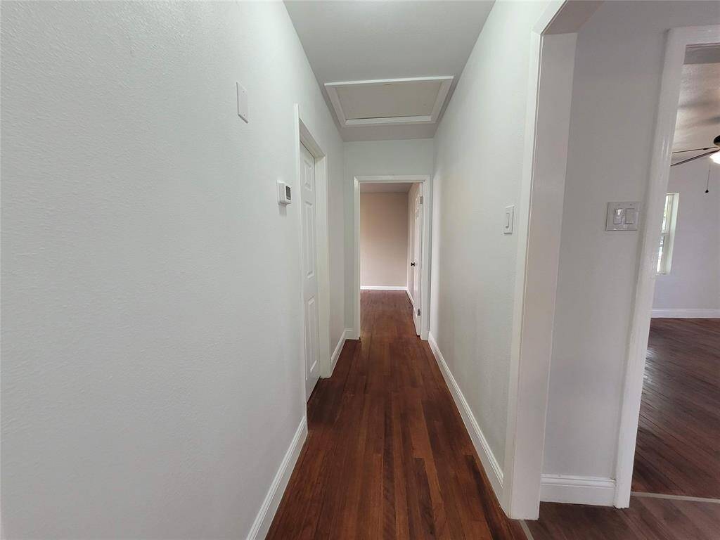 A bright, clean hallway with hardwood floors and white walls, leading to multiple rooms. The space feels open and well-maintained.