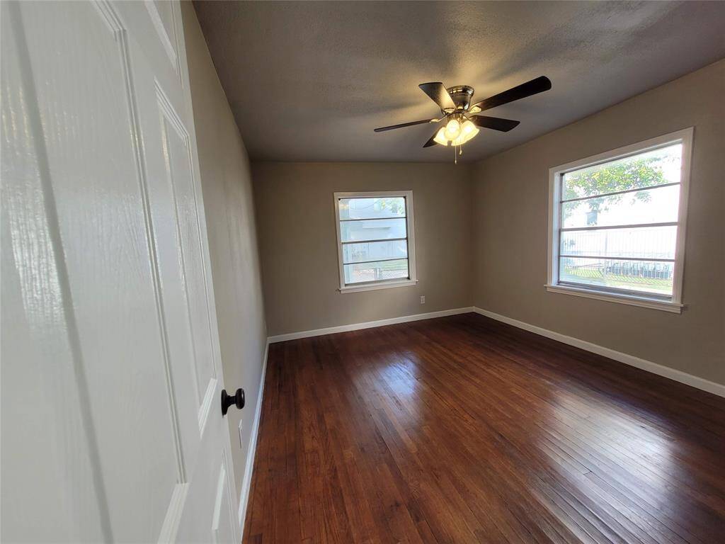 Bright bedroom with wood flooring, neutral walls, and a ceiling fan. Features two large windows providing natural light.