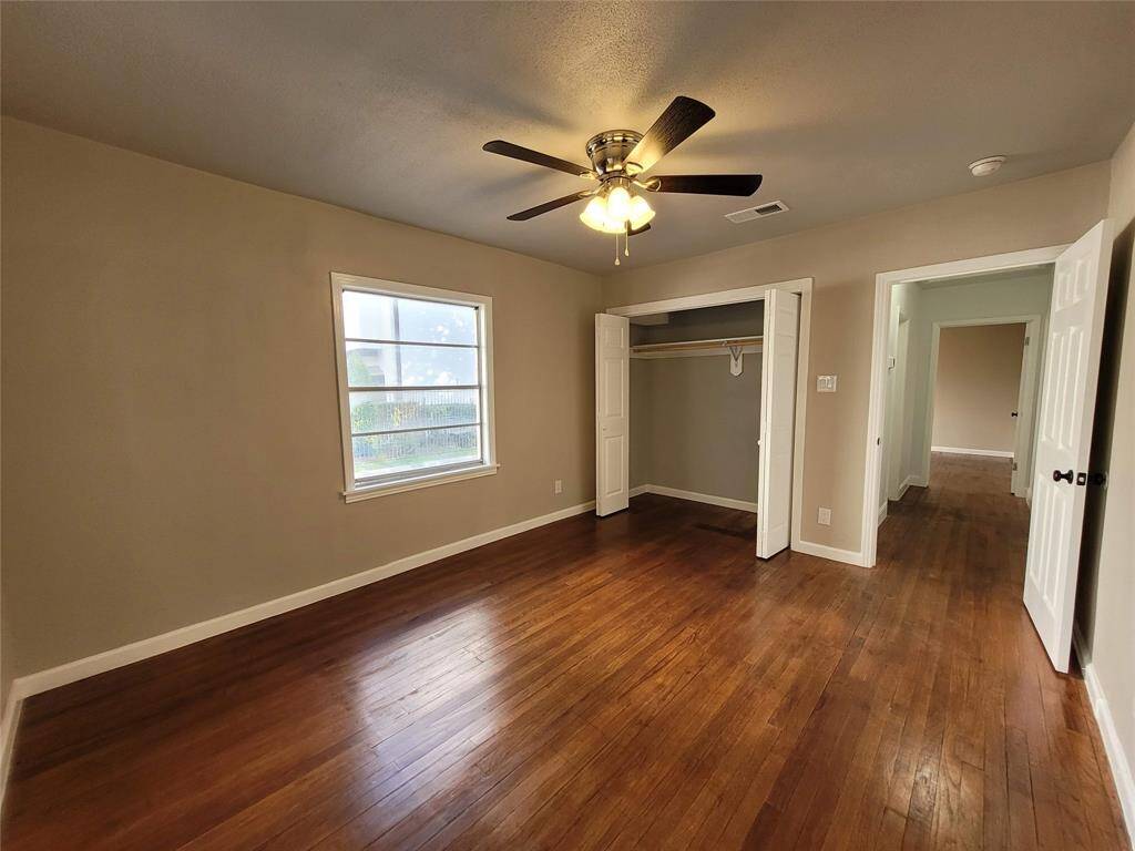 This room features warm hardwood flooring, a ceiling fan with lighting, a spacious closet with double doors, and a large window providing natural light.