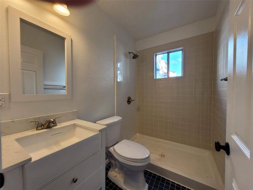 Bathroom featuring a walk-in shower with beige tiles, a modern sink with a marble countertop, and a window for natural light.