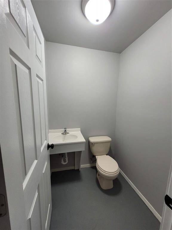 This is a compact half-bathroom with a simple design, featuring a toilet and a small wall-mounted sink. The walls are painted a light gray, and the room has a ceiling light for illumination.